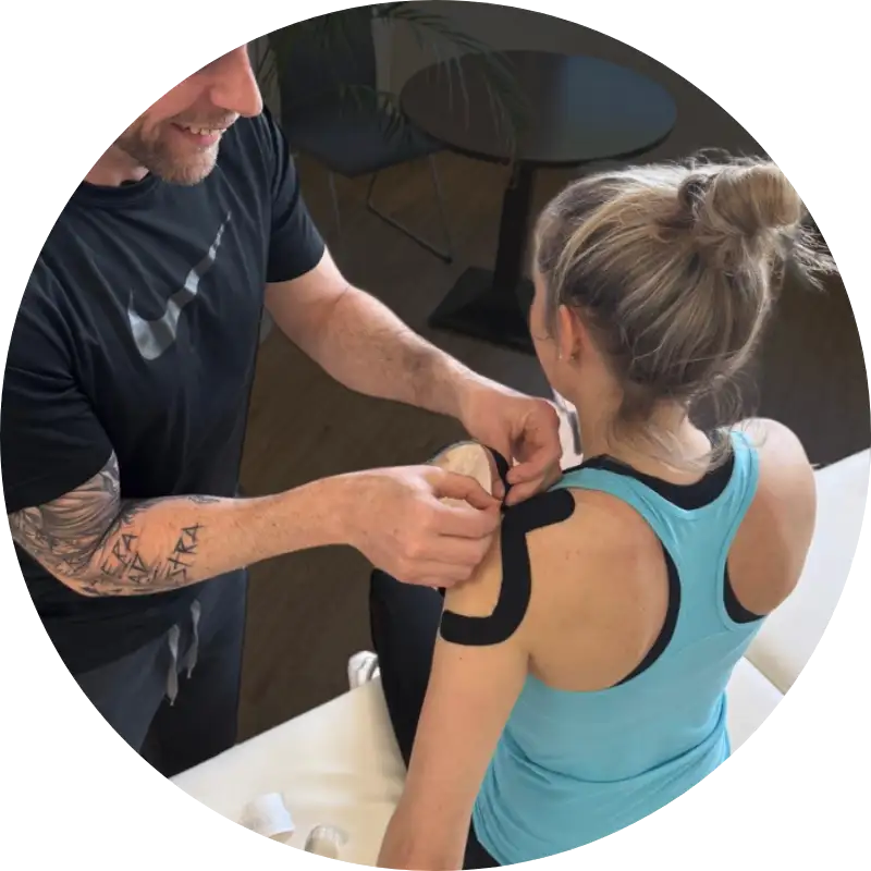 Kinesiologisches Taping in der Sporttherapie Sporttherapeut bringt schwarzes Kinesiotape auf der Schulter einer Patientin an.