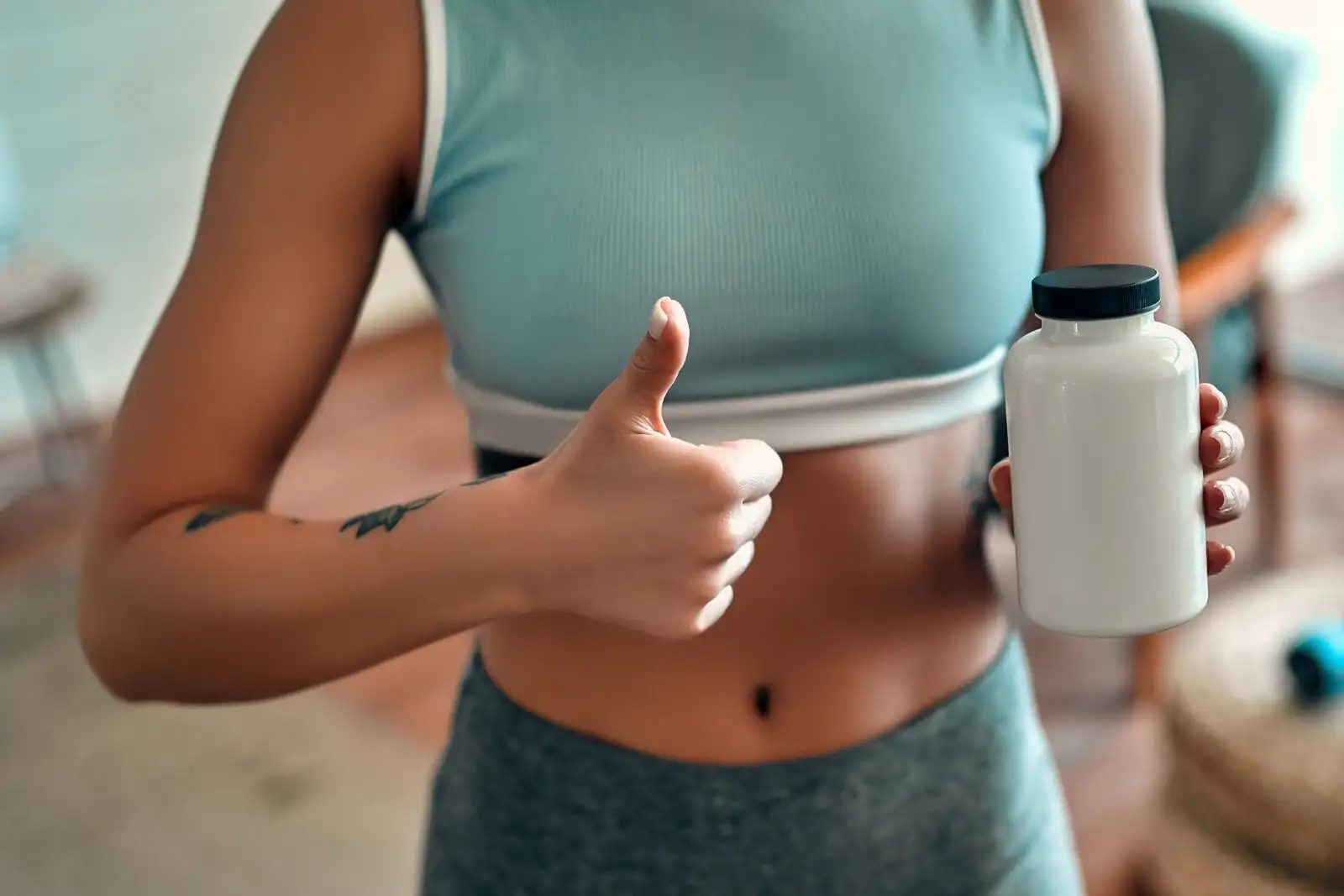Fitness-Support mit System – Daumen hoch für gesunde Routinen Sportlerin zeigt Daumen hoch und hält eine weiße Supplement-Flasche – Symbol für gesunden Lebensstil.